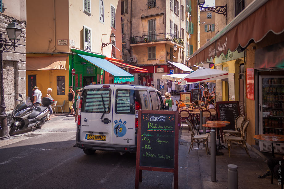 People, motorollers, tables and cars share the streets of Nice